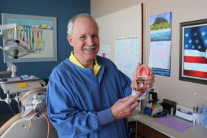 Dentist Dr. William Hartman holding a model showing how dentures work when creating custom same-day dentures