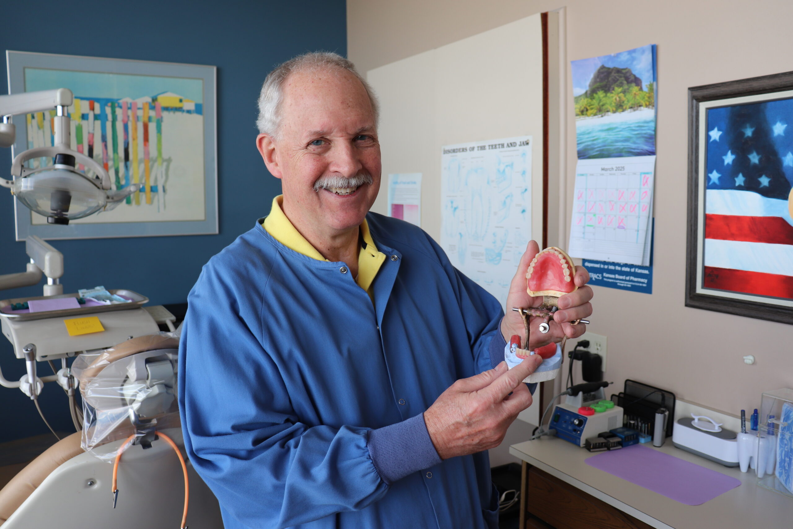 Dentist Dr. William Hartman holding a model showing how dentures work when creating custom same-day dentures